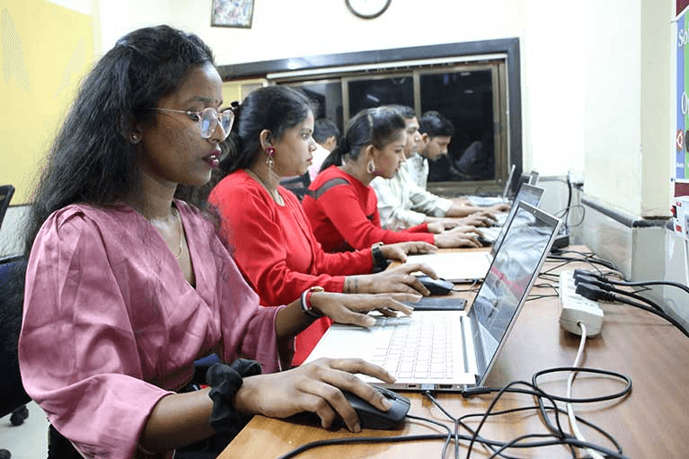 A row of Indian women sitting at desks and learning in a computer laptop laboratory setting